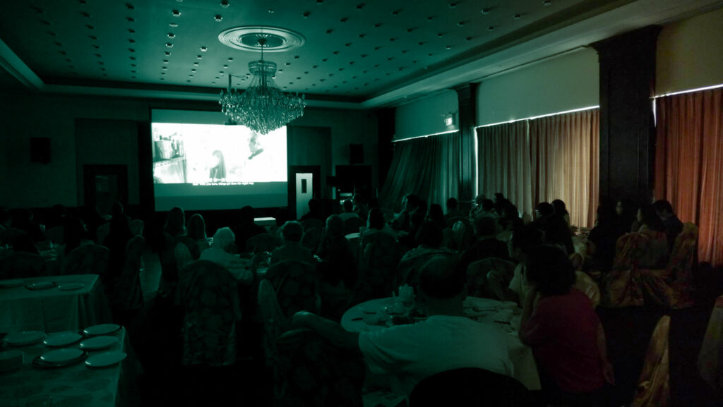 Film Screening in a Dim Sum Restaurant. People at tables watching movie.