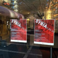 Posters advertising Syria Speaks event in window.