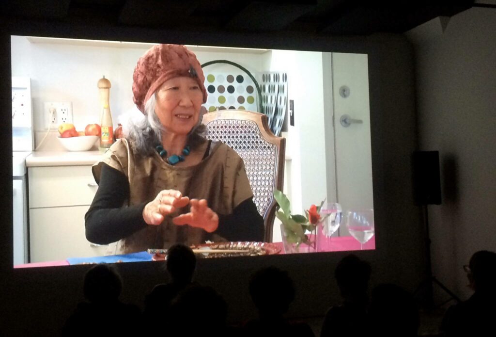 Event image from Art Talking Women Launch event at VIVO. On the screen is an image of Tsuneko Kokubo, speaking at a kitchen table.
