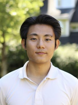 Headshot of Daniel Chen. He is outdoors. His white collared shirt stands out against the greenery in the background. His face is soft and his gaze warm as he smiles.