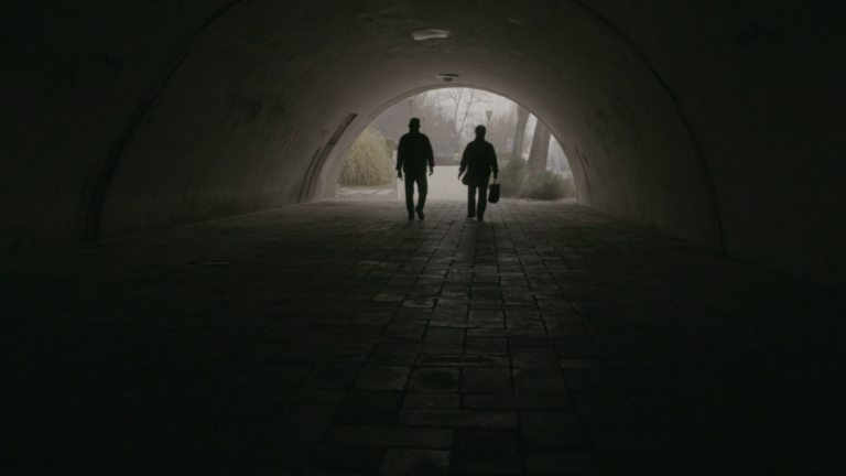 Mister and missus Deng walking together through a dark tunnel towards the light.